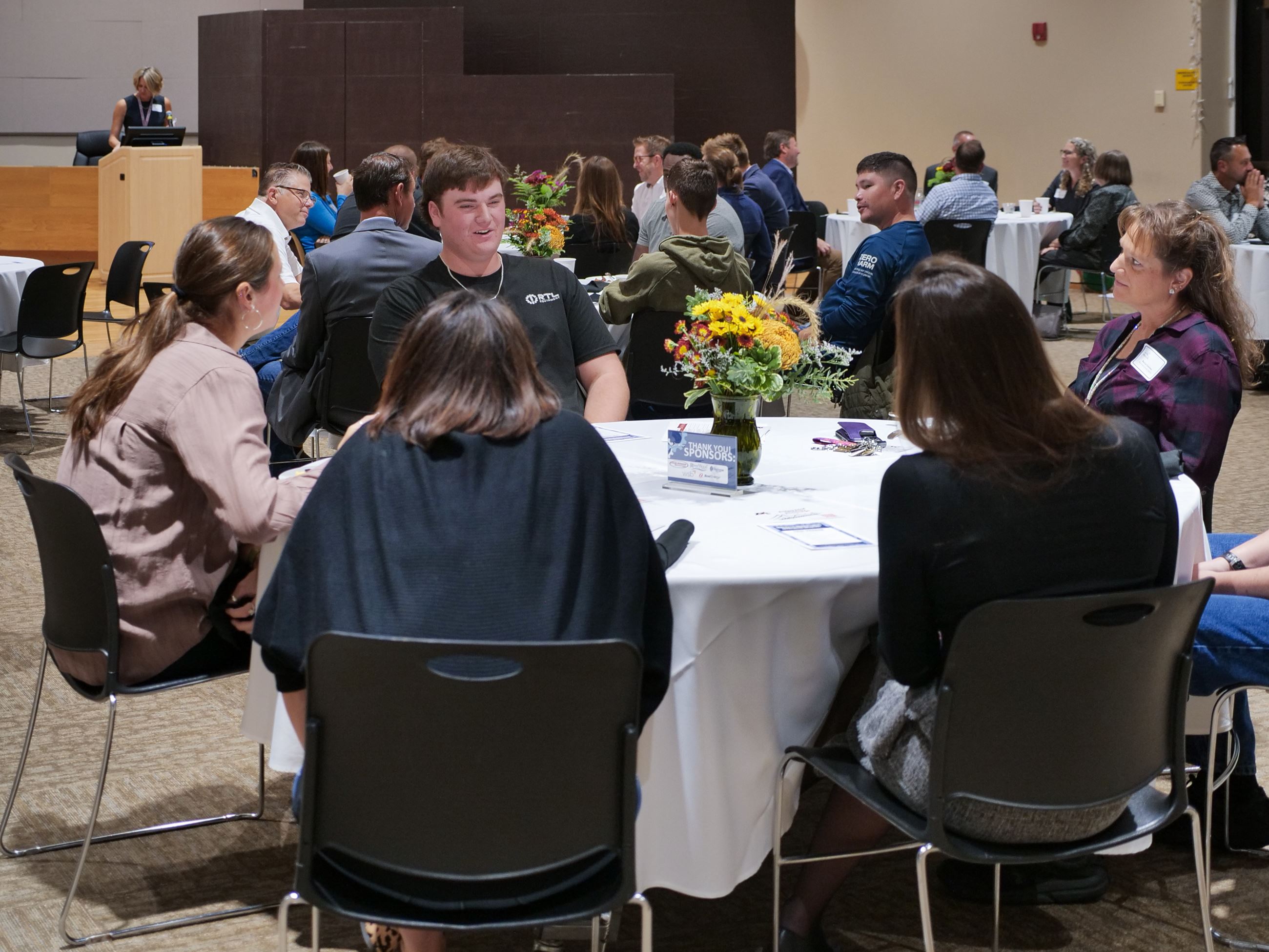 Manufacturers Breakfast table speaking with high school student.
