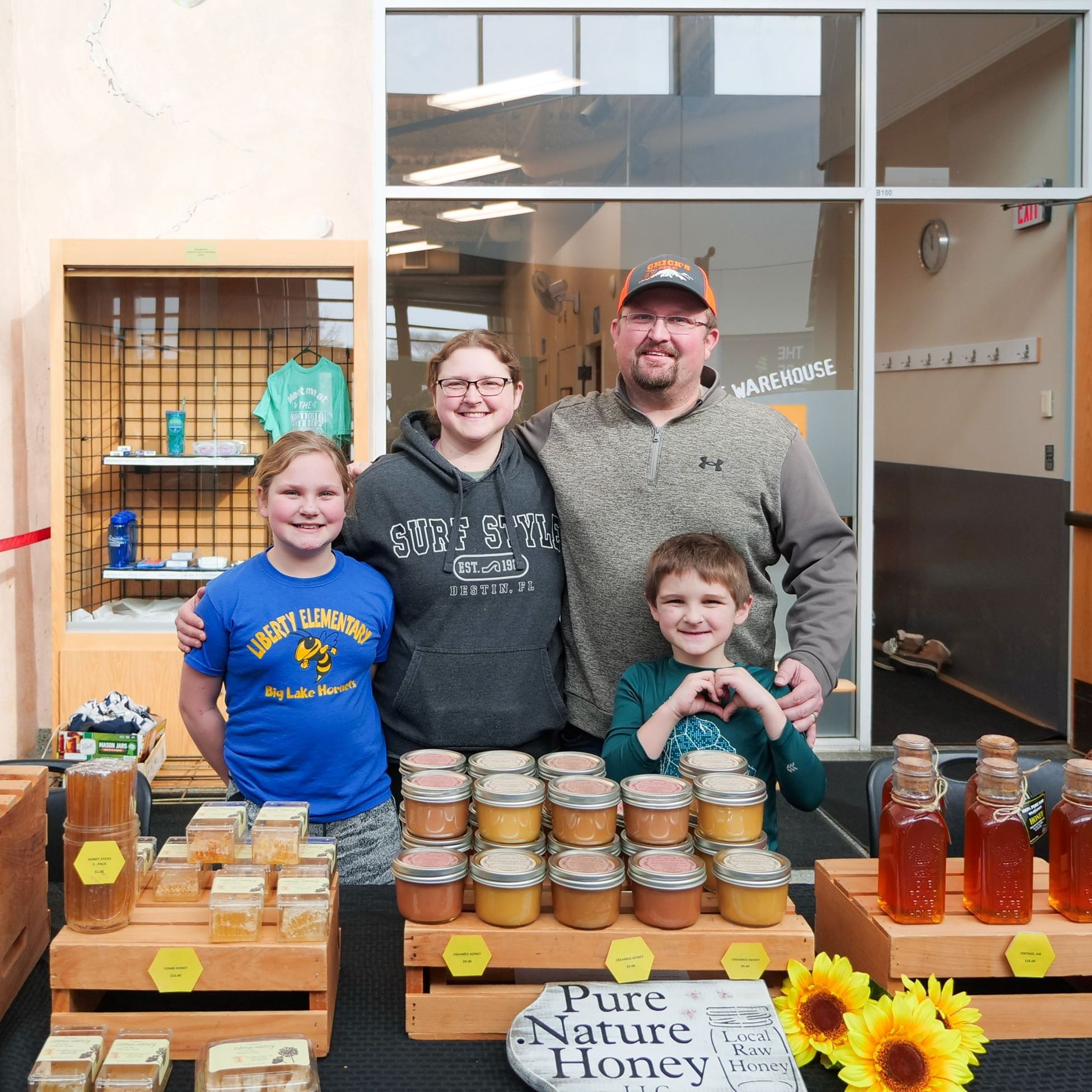 Family behind table selling local honey at the indoor Farmers Market.
